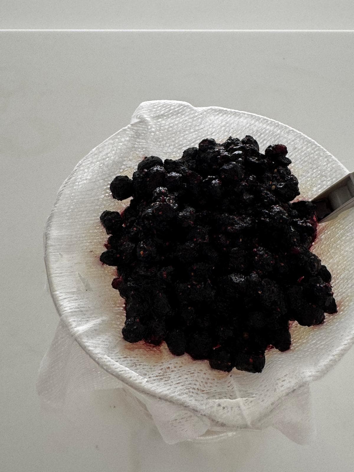 Frutas silvestres escuras amontoadas sobre um pano de gaze branco em uma superfície clara.